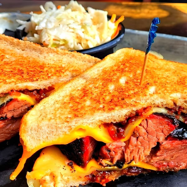 Fat Pete's BBQ brisket grilled cheese sandwich with melted cheese, served with coleslaw.