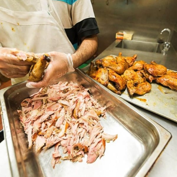 Chef wearing gloves shreds BBQ chicken into a metal pan, with whole chicken pieces nearby.